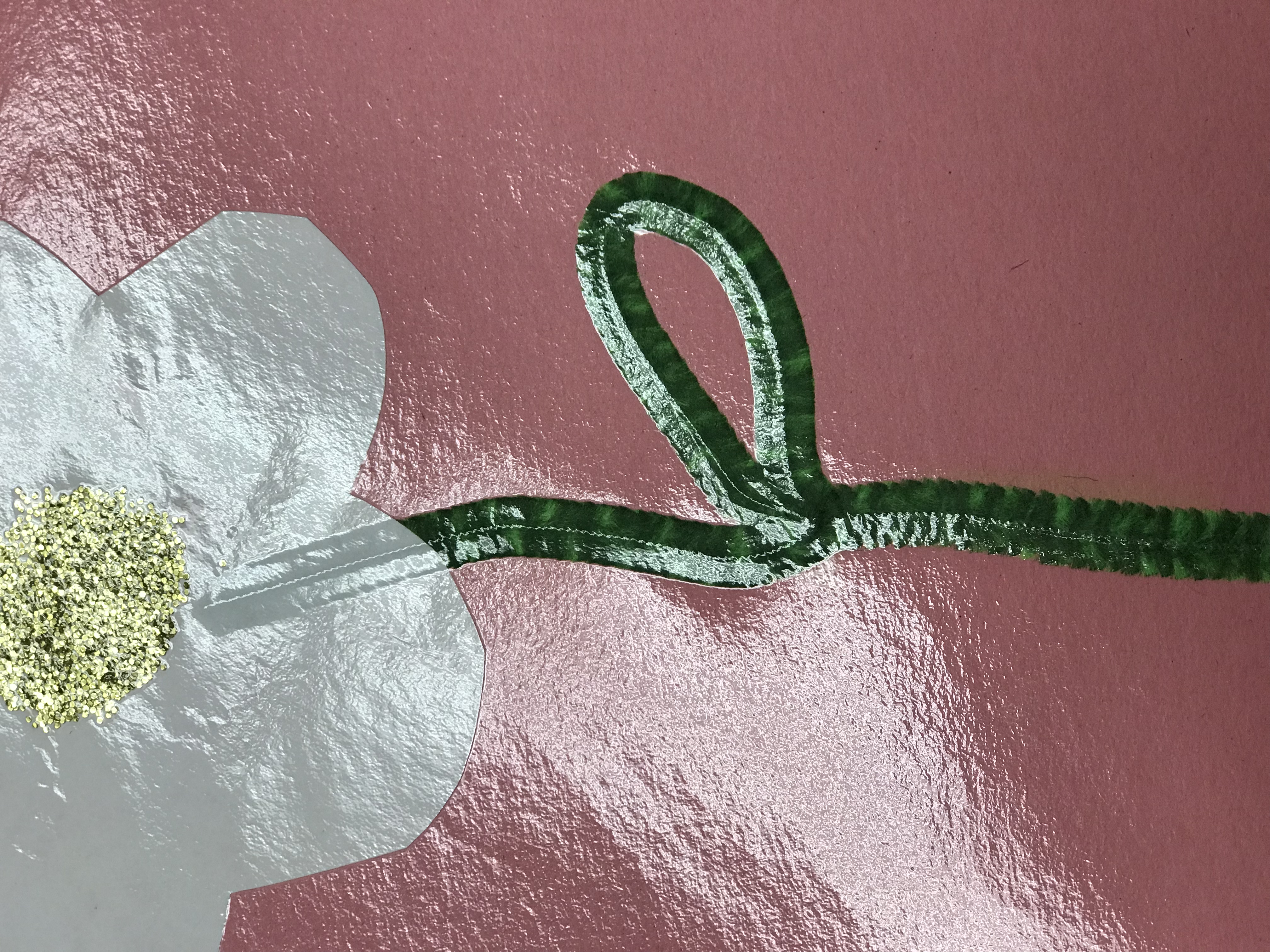 Laminated white paper flower with green pipe cleaner stem on pink paper