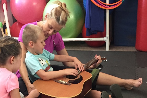 Two kids and an adult woman practicing guitar