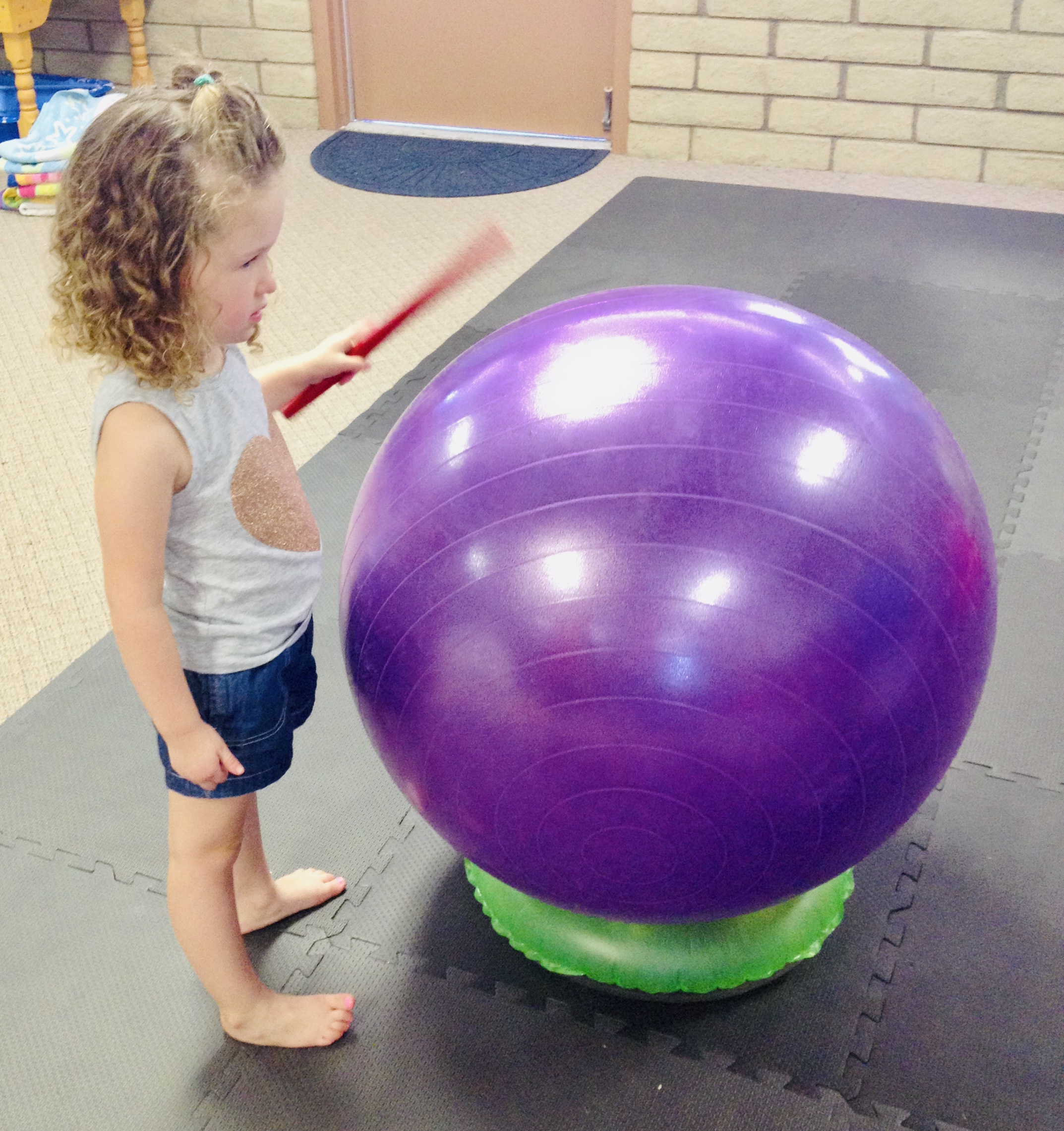 Little girl hitting drumstick on yoga ball