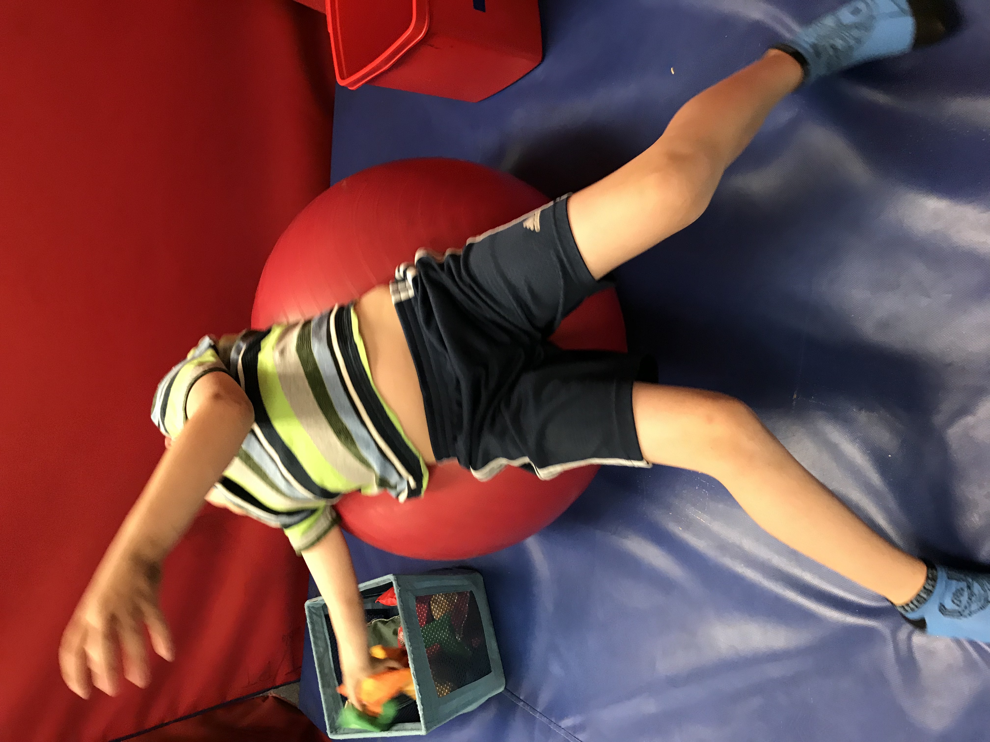 Boy reaching into bin while laying on yoga ball